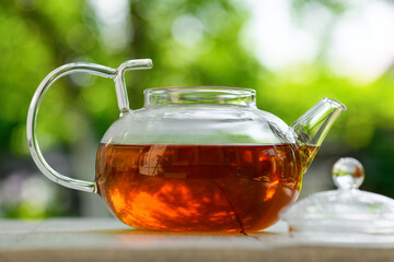 Tea in a glass teapot on a green background. Teapot with green or black tea with reflection in glass in the country. Tea time