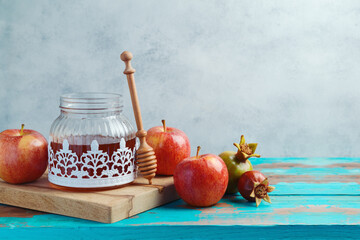 Vintage honey jar, red apples and pomegranate on wooden blue table. Background for Jewish holiday Rosh Hashanah
