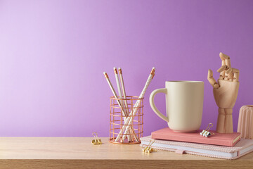 Stylish feminine home office desk with coffee cup, notebook and pencils over purple background....