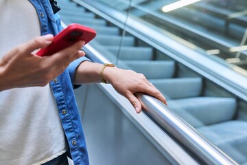 Close-up of a womans hand with smartphone on an escalator, in modern building