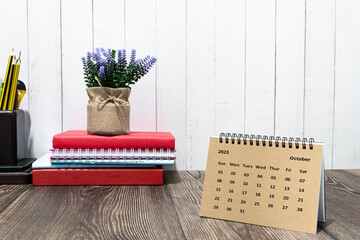 Brown October 2023 calendar on wooden desk with office stationery.