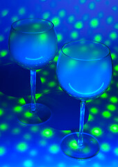 Two glasses with an alcohol vapors of vodka in a blue light on a blue background. Scene is covered with plenty of green dots. Selective focus.
