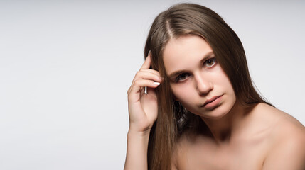 A young, attractive girl with beautiful, long, straight hair, brown eyes and bare shoulders. Close-up portrait. Free space for text advertising