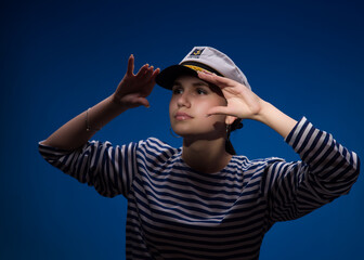 A young, attractive girl with brown eyes in a vest and a captain's cap on a blue background. Close-up portrait. Free space for text advertising