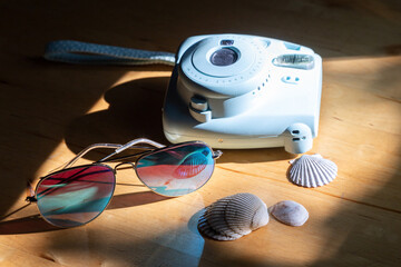 Horizontal selective focus still life with a summer vacation vibe, including retro style camera, turquoise sunglasses and shells on wooden background