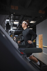 Fototapeta na wymiar Vertical shot of a handsome athletic man running on treadmill at the gym