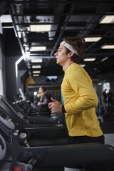 Fototapeta na wymiar Vertical profile shot of a male athlete wearing headband, running on treadmill at gym