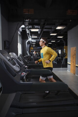 Fototapeta na wymiar Vertical full length shot of a male runner on a treadmill at the gym