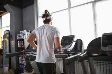 Rear view shot of a male athlete working out at the gym, running on treadmill