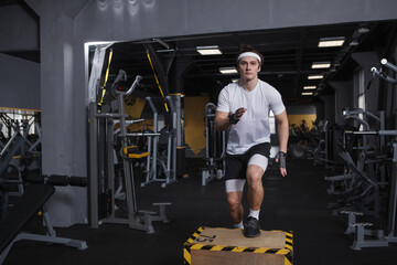 Sportsman wearing headband stepping on a box, exercising at gym