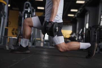 Fototapeta na wymiar Cropped shot of unrecognizable athletic man doing lunges with dumbbells at gym