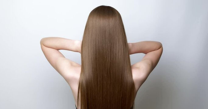A woman with her hands shows beautiful and long hair on a white background.