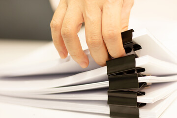 Close-up of woman hand pick up stack of report papers document with paper clip and laptop....
