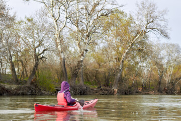 Woman in red kayak paddle at river near gentle spring trees