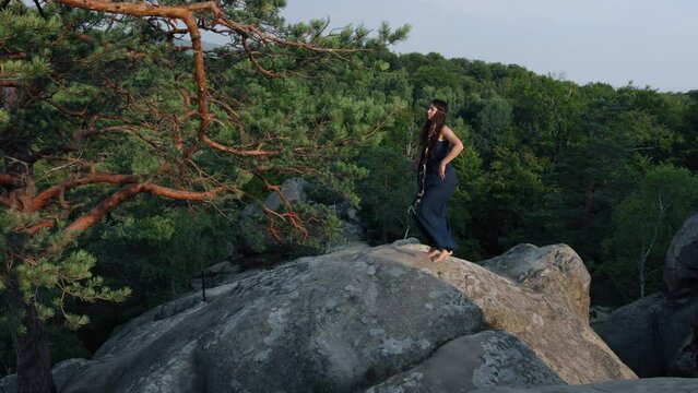 Young female in blue dress on edge of a cliff. Mystic pictures, ballet dancer stands on cliff end. Woman in beautiful gown standing on edge of the rock.