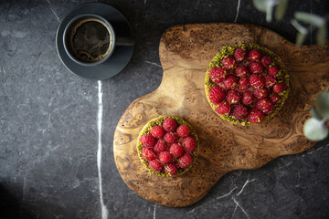 Top view on raspberry tartlets with pistachios and coffee on serving board