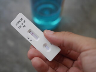 Close-up photo of hand holding Antigen test kit showing results of testing for COVID-19 test result is negative, with alcohol backdrop, ideal for illustrating COVID-19 news.
