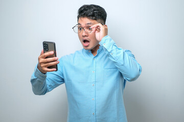 Shocked young good looking Asian man using smartphone to read good news online isolated