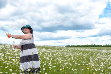Grandmother blows soap bubbles in a field of daisies.