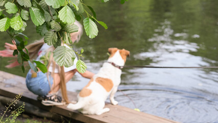 girl sitting near the lake with her dog. back view of a girl with her pet friend looking at water. friendship and pet care, walking and traveling with animals.