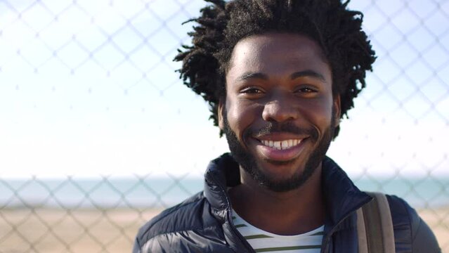 Portrait of confident black man with trendy afro enjoying the view of the city against a fence background with copyspace. African american student looking happy while taking a relaxing walk downtown