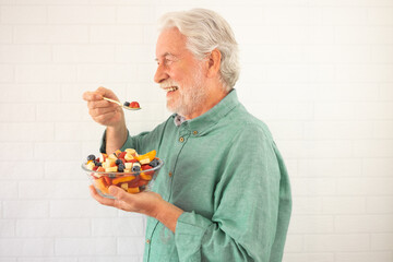 Smiling senior white-haired man ready to eat a salad of fresh summer fruits. Breakfast or lunch...