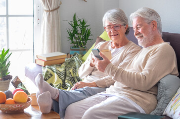 Senior couple relaxing on sofa at home looking together at smart phone. Lifestyles retirement concept