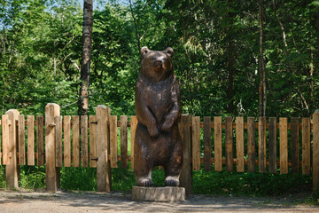Fototapeta na wymiar Sculpture of full-length wooden brown bear in park on stump. concept of travel in Russia. Kivach Nature Reserve in Karelia.