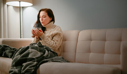 Young woman sick with flu with a cup of hot cough tea blowing on him. Winter cold concept.