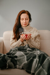 Woman sick with the flu sits at home in quarantine drinking hot tea keeping warm in winter.