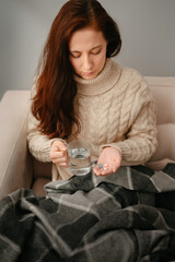 Young woman at home treats illness with pills. Headache or flu during the winter season.