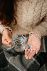 Woman holds in her hands a glass of water and three pills for colds and flu. Antibiotic treatment concept.