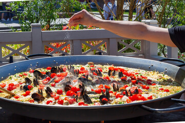 Cooking typical spanish seafood paella in traditional pan with man's hand to salt.