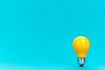 Yellow bulb standing on turquoise background with copy space. Minimalist photo of lightbulb over...