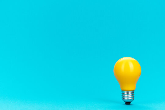 Yellow bulb standing on turquoise background with copy space. Minimalist photo of lightbulb over blue.