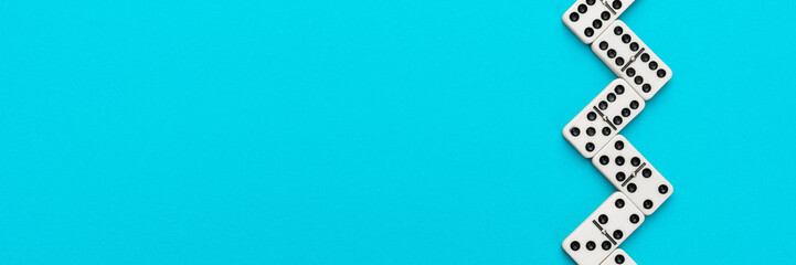Domino pieces forming zigzag on turquoise blue background with copy space. Flat lay minimalist...