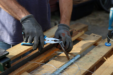 Man holds pliers and steel wire. Handyman tools close up photo. Male hands in grey protective gloves. 