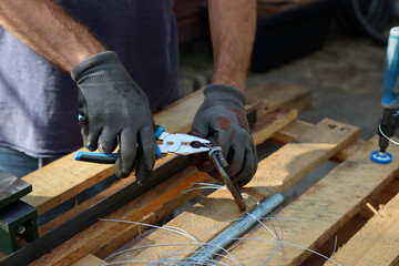 Man holds pliers and steel wire. Handyman tools close up photo. Male hands in grey protective...