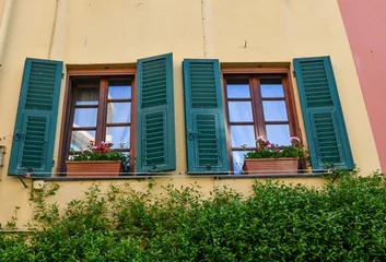 Poster Low-angle view of a pair of windows with potted geraniums on the sills and green shutters, Boccadasse, Genoa, Liguria, Italy © Simona Sirio