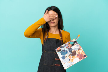 Young artist caucasian woman holding a palette isolated on blue background covering eyes by hands....