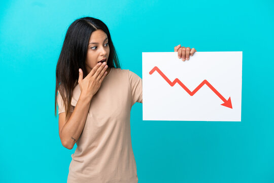 Young woman over isolated background holding a sign with a decreasing statistics arrow symbol with surprised expression
