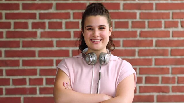 Portrait of a sporty young woman against a red brick wall with copy space. Confident female athlete listening to music while exercising or working out. Happy girl training for cardio and endurance