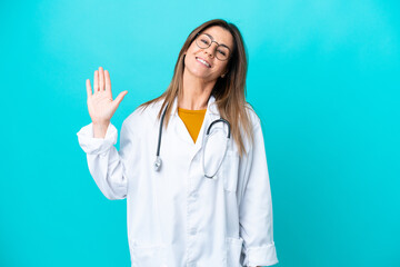 Middle age woman isolated on blue background wearing a doctor gown and saluting
