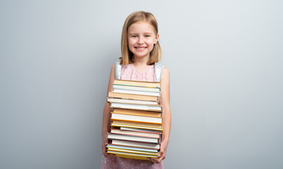 Little girl with backpack and textbooks stack on gray background