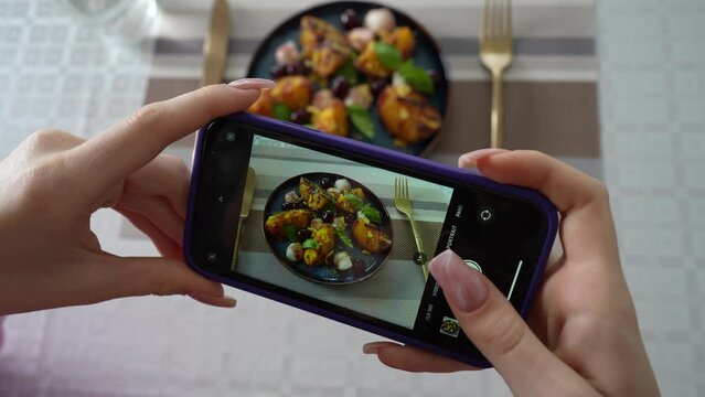 Girl take pictures of grilled peach salad with mozzarella, using smartphone. Female hands take photos of food by modern smartphone. Close up, 4K