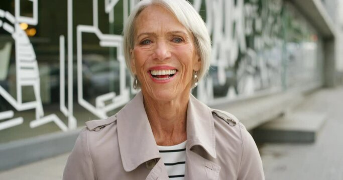 Portrait of smiling senior woman out traveling in the urban city. Confident and positive mature lady with grey hair laughing and having fun outdoors. Showing dentures and cheerful facial expression