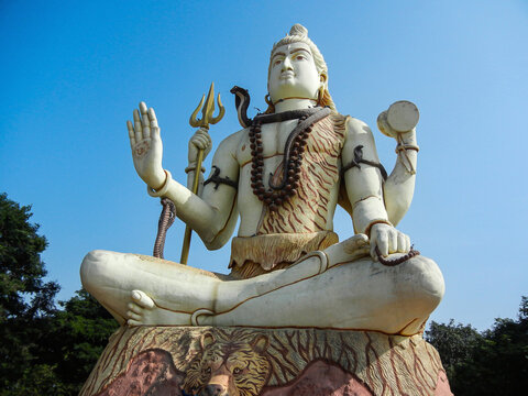 Stock photo of 25 meter tall giant white color lord shiva idol in sitting position blue sky on background. Picture captured under bright sunlight at Dwaraka, Gujarat, India. blue sky on background.