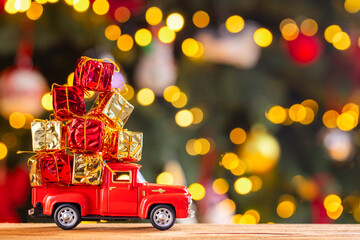 Red retro toy truck carries gifts on the background of Christmas tree with christmas lights. Concept of delivery of goods and a greeting card happy New year