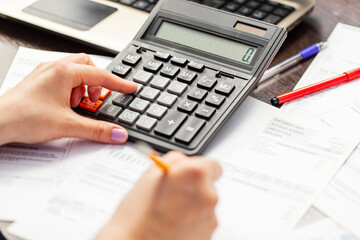 Woman using using calculator for calculate home finances or car taxes, woman managing home family expenses using calculator, making payment on laptop
