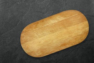 Top view of an empty wooden cutting board on a dark slate stone background.